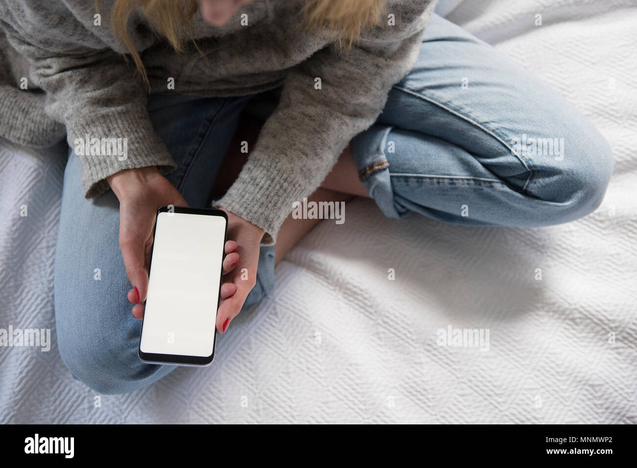 Frau sitzt im Bett mit Smartphone Stockfoto