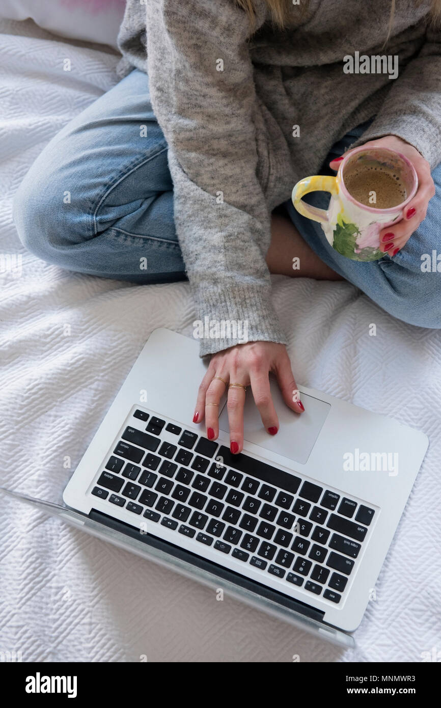 Frau mit Kaffee und Laptop im Bett Stockfoto