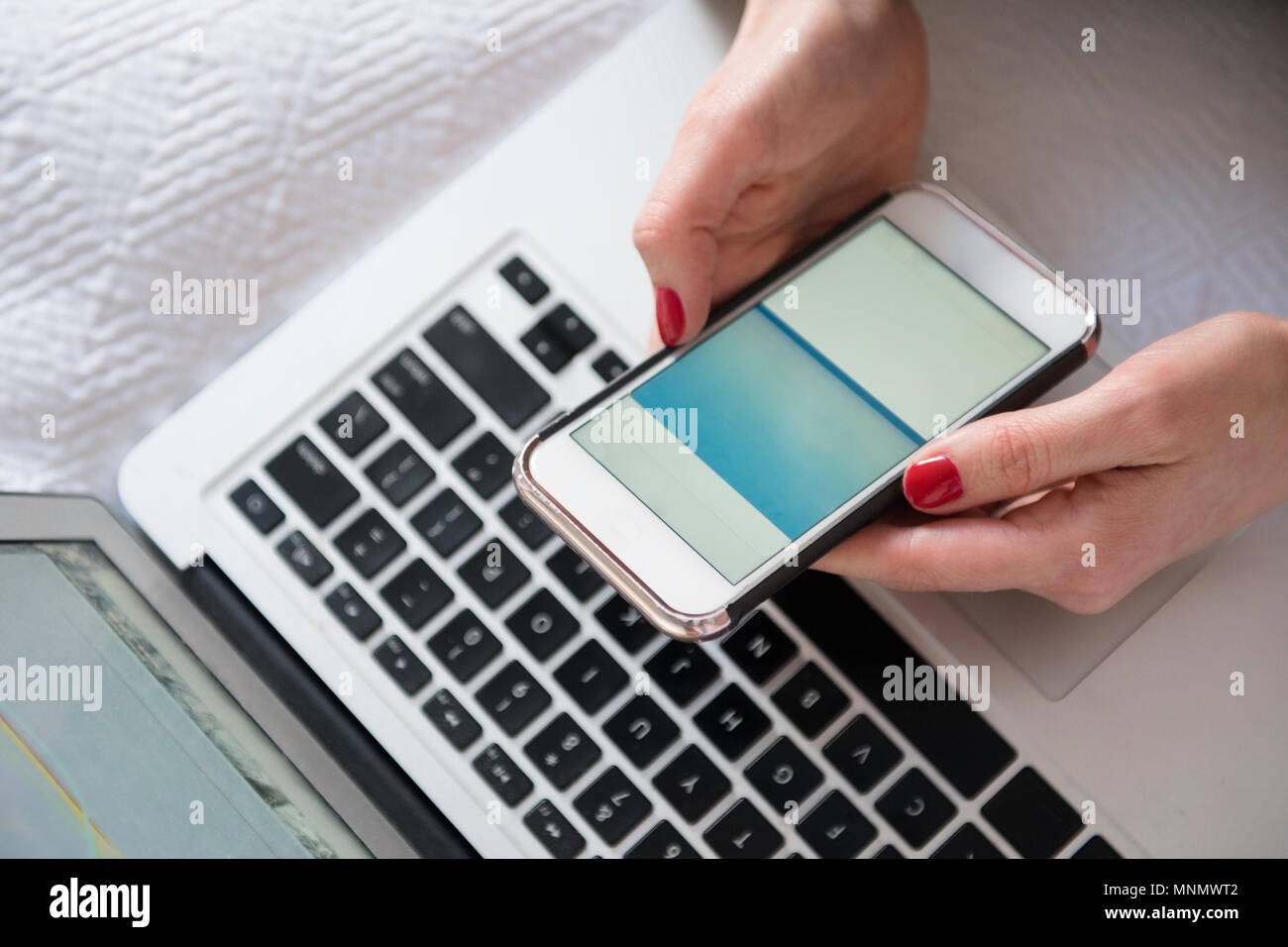 Frau mit Smartphone und Laptop im Bett Stockfoto