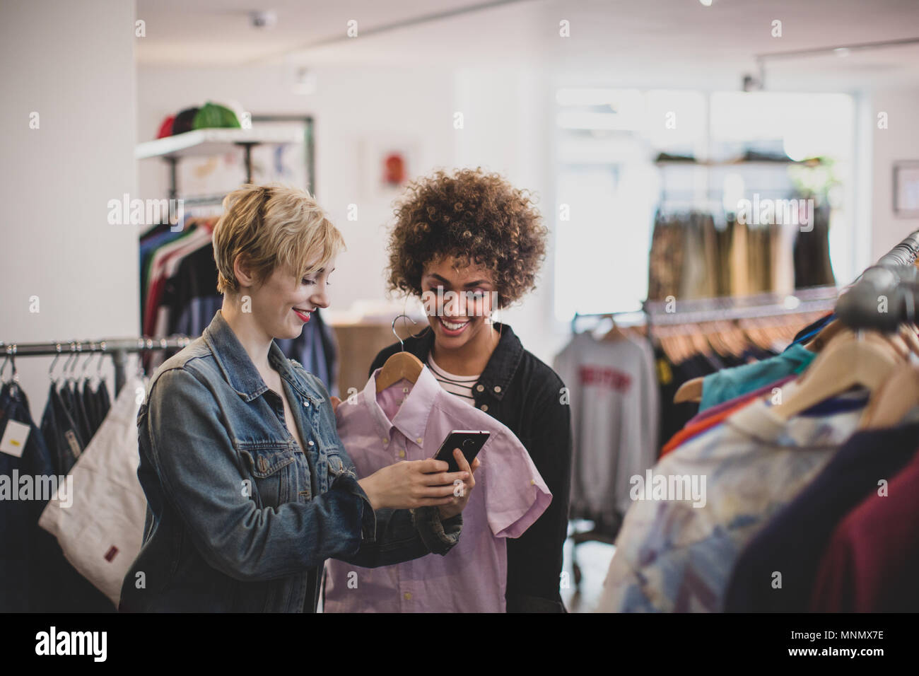 Tausendjährige weibliche Freunde auf der Suche nach einem Smartphone in einem vintage Clothing Store Stockfoto