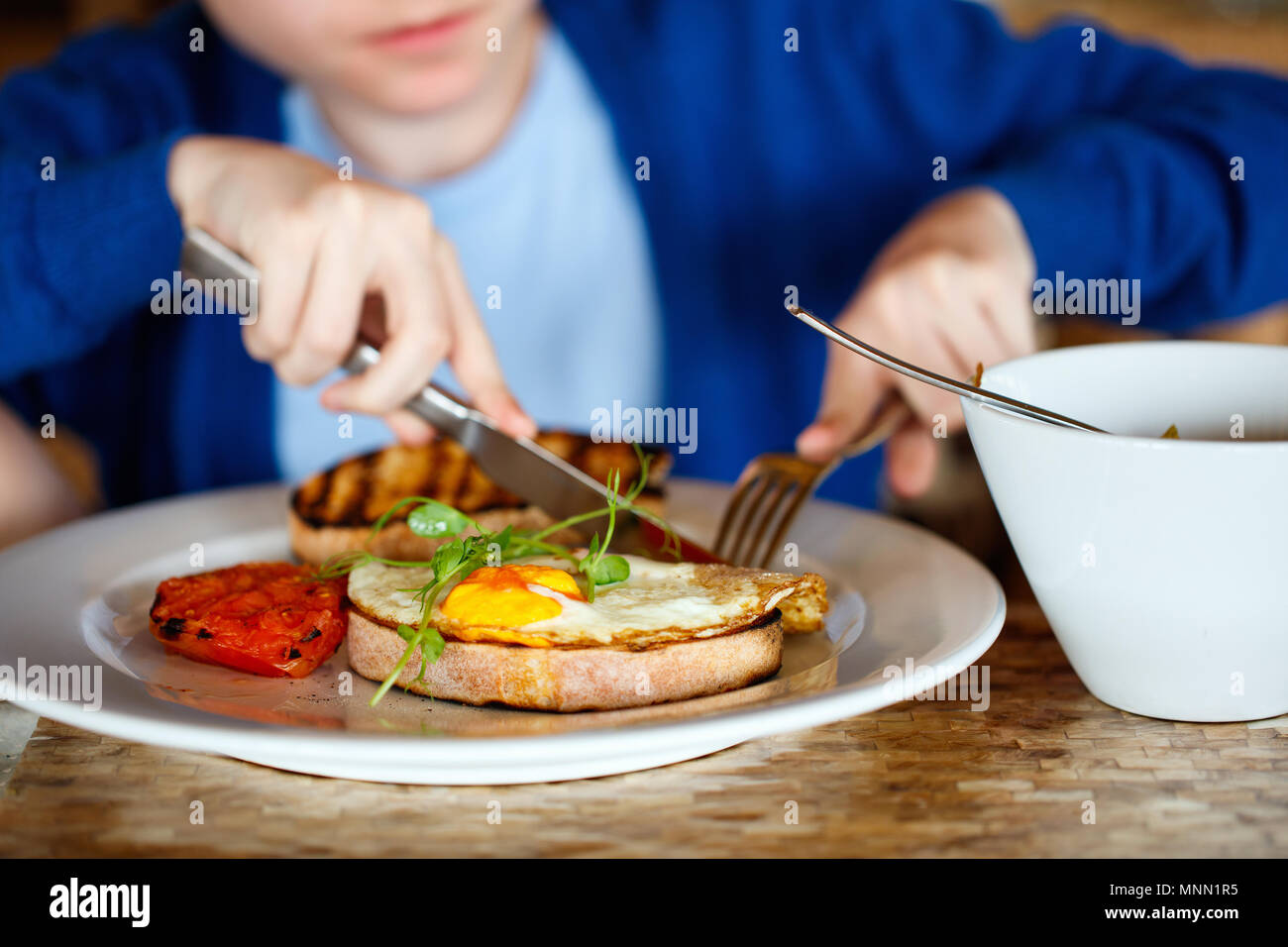 Junge essen Spiegelei auf Toast und Porridge zum Frühstück Stockfoto