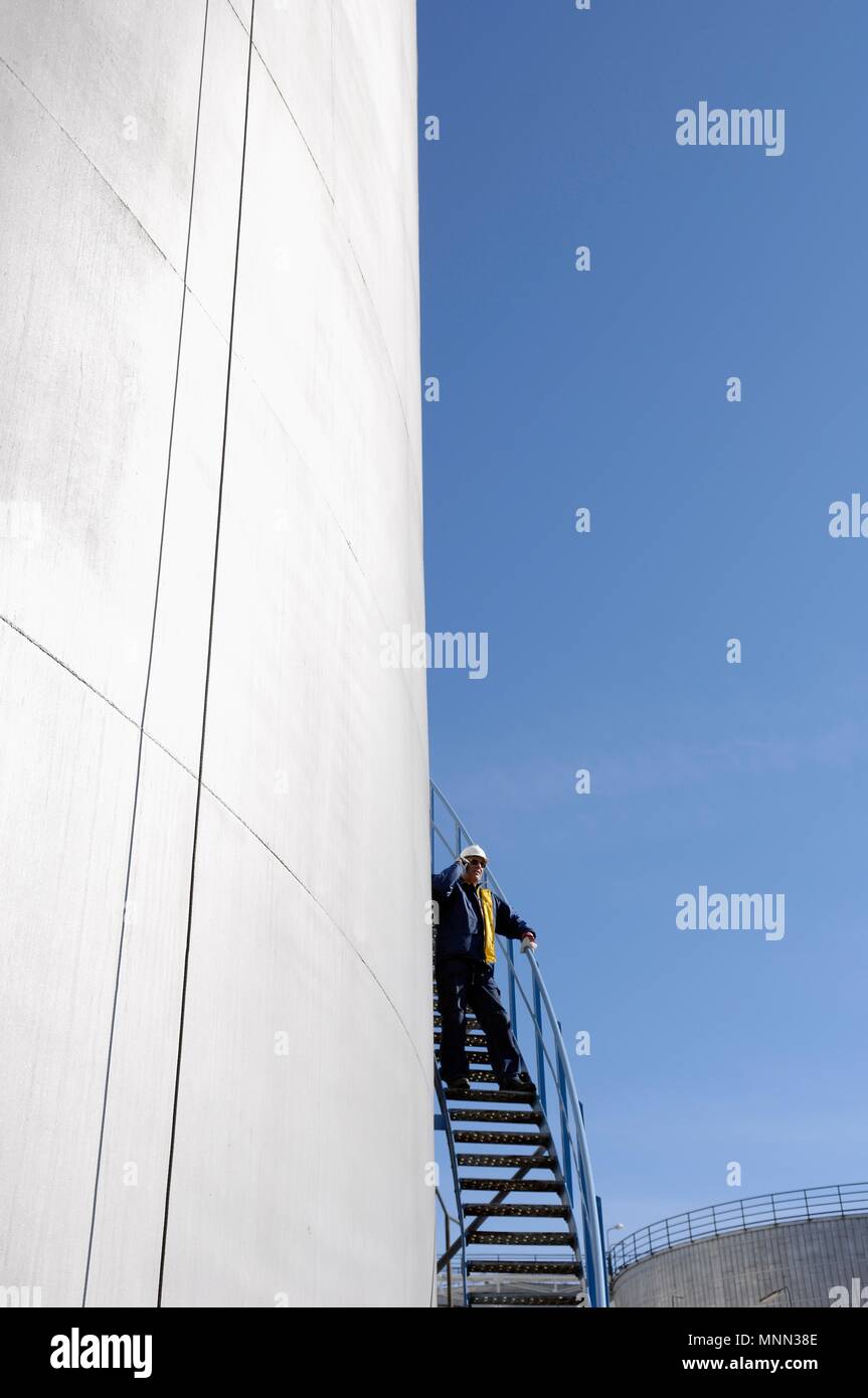 Raffinerie Arbeiter stehen auf der Leiter am Telefon sprechen neben  Industrie, Öl und Kraftstoff Lagertanks Stockfotografie - Alamy