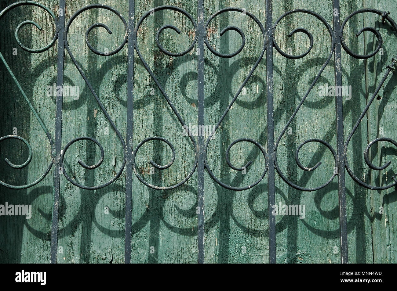 Curlicue Schmiedearbeiten und Schatten auf dem alten grünen Holz Wand in New Orleans Stockfoto