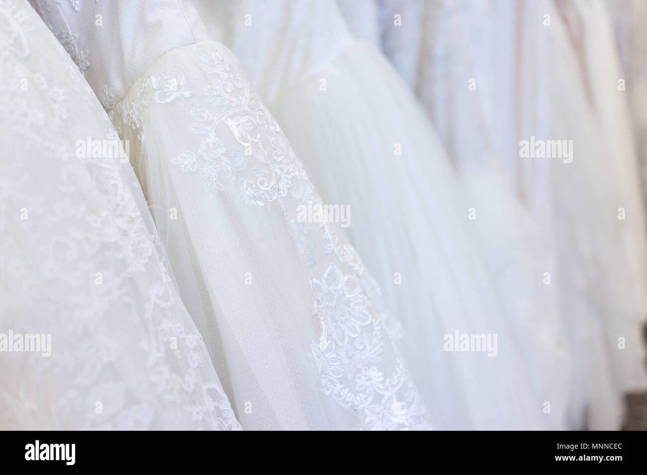 Viele Brautkleider in Boutique Diskontgeschäft, weiße Kleider hängen an Rack Kleiderbügel Reihe Nahaufnahme mit weißer Spitze, Tüll, Design Stockfoto