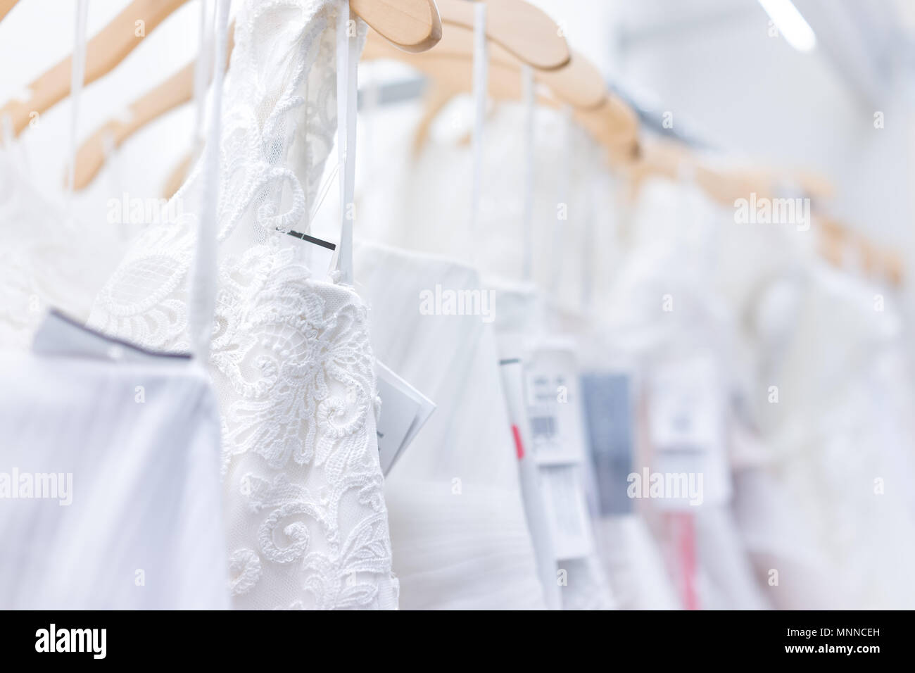 Viele Brautkleider mit Preisschildern in Boutique Diskontgeschäft, weiße Kleider hängen an Rack Kleiderbügel Reihe Nahaufnahme mit weißer Spitze, Tüll, Design Stockfoto