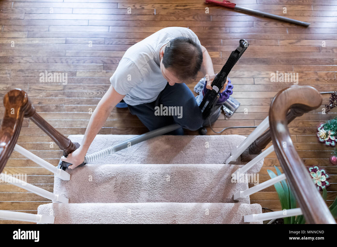Junger Mann Haus Mann bleiben zu Hause Vati Staubsaugen mit Vakuum auf dem Teppich boden, Innen, Innere des Haus Wohnzimmer Eingangsbereich, sitzen auf den Treppen, Stockfoto