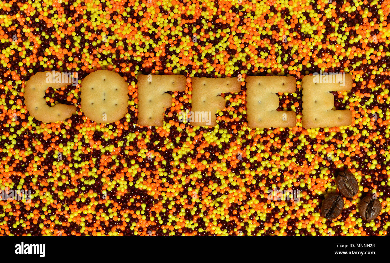 Kaffee. Das Wort von den essbaren cracker Buchstaben liegt auf der verglasten Pulver. Eine große Anzahl von süßen, bunten Perlen von sehr kleinen Größe für die Dekoration Stockfoto