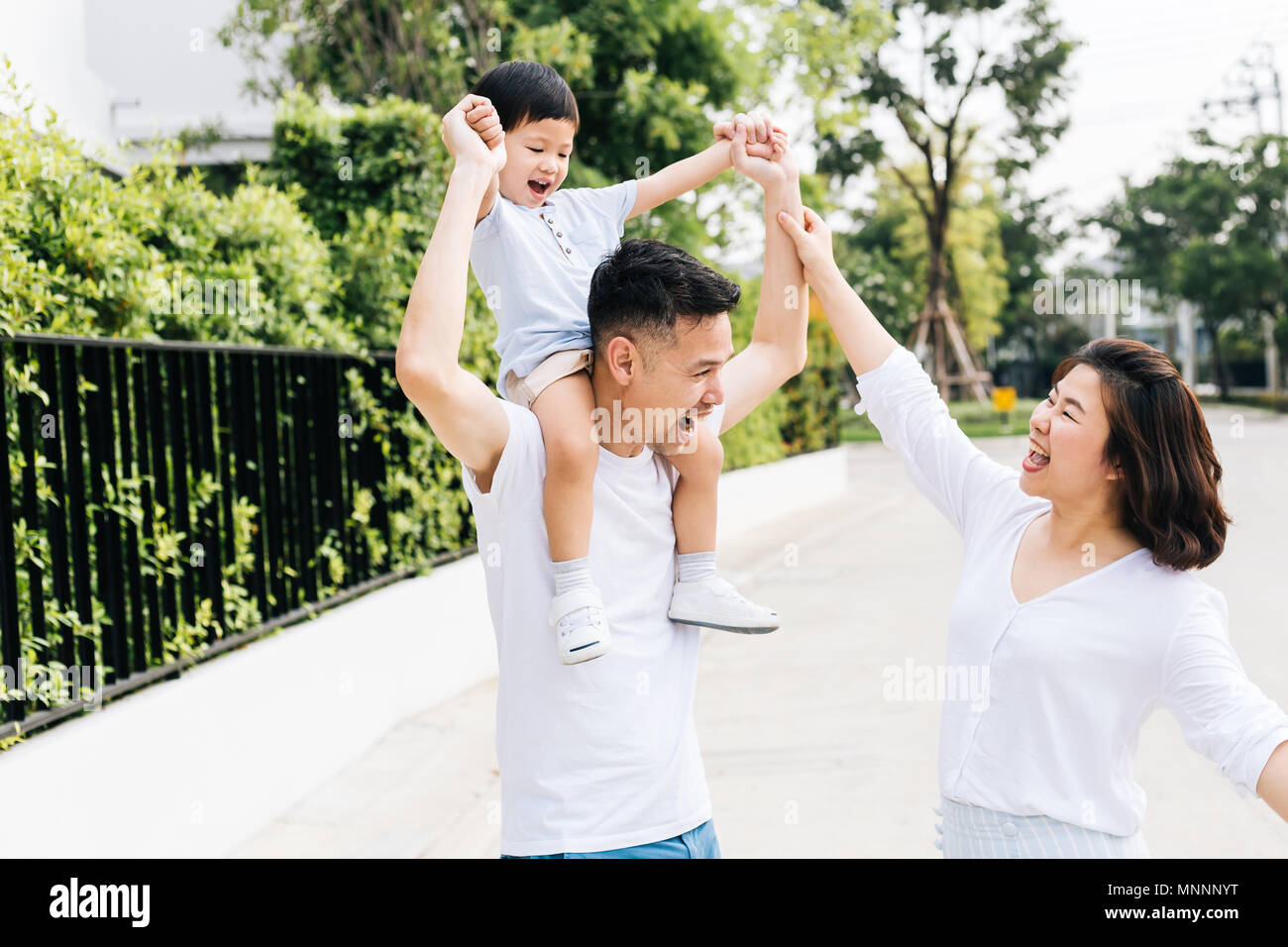 Cute Asian Vater huckepack sein Sohn zusammen mit seiner Frau im Park. Familie begeistert die Hände zusammen mit Glück Stockfoto