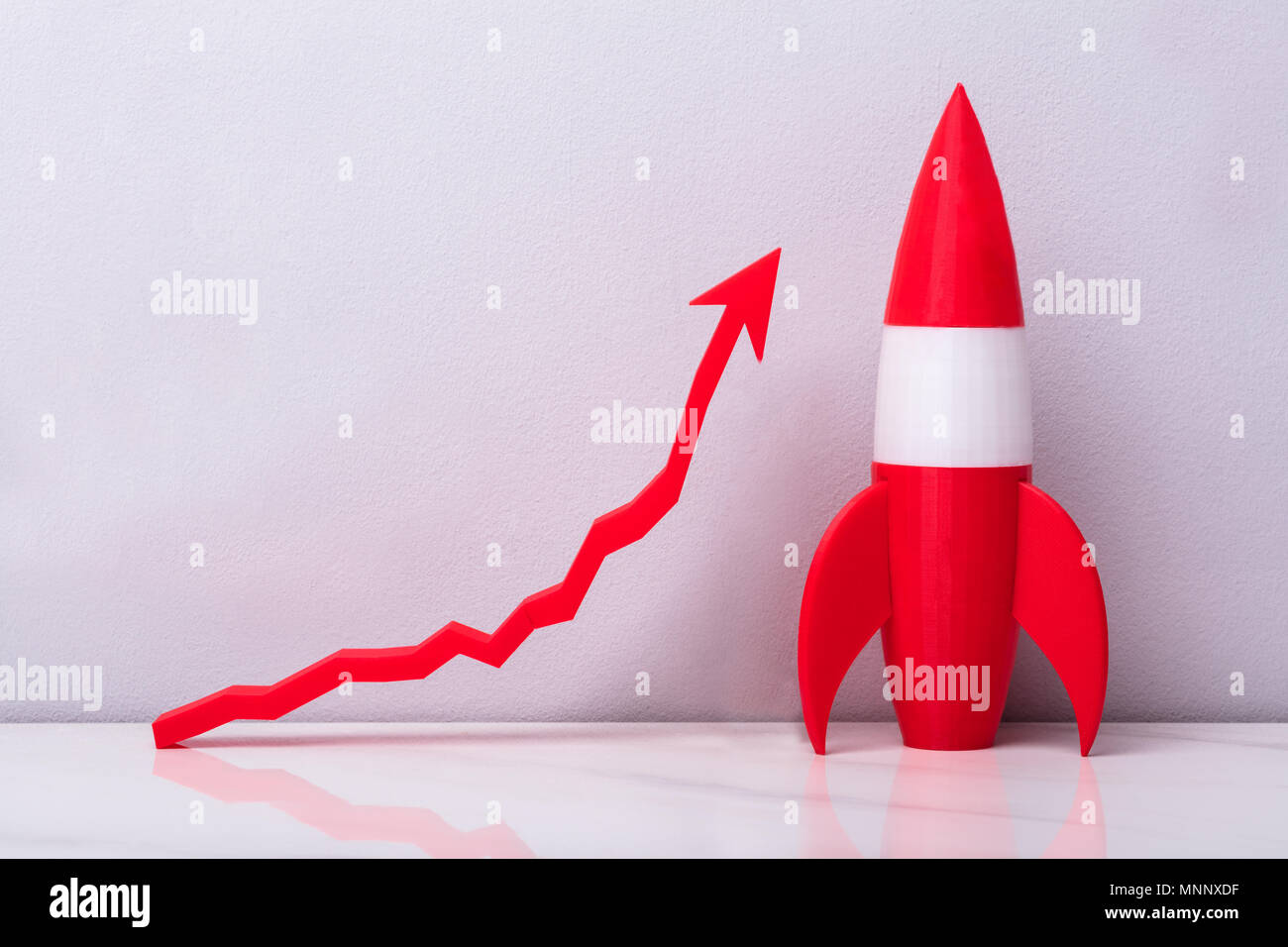 Red Rocket in der Nähe von White steigende Pfeil Graph auf grauem Hintergrund Stockfoto