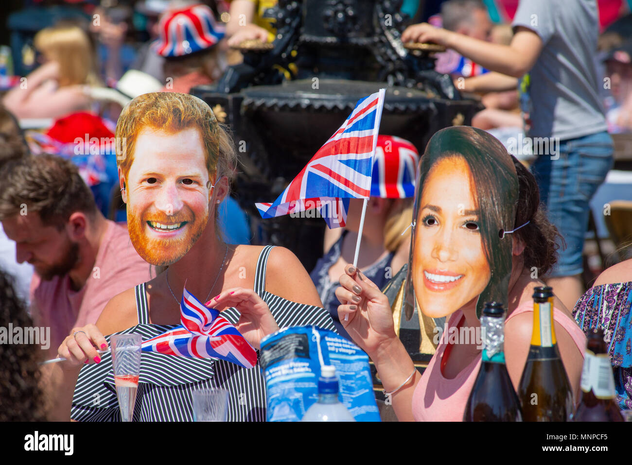 Menschen mit Gesichtsmasken von Prinz Harry und Meghan Markle und winkenden Union Jack Flaggen auf einer Straßenparty, um die königliche Hochzeit zu beobachten und zu feiern. Ringwood, Hampshire, England, Großbritannien, 19.. Mai 2018. Stockfoto
