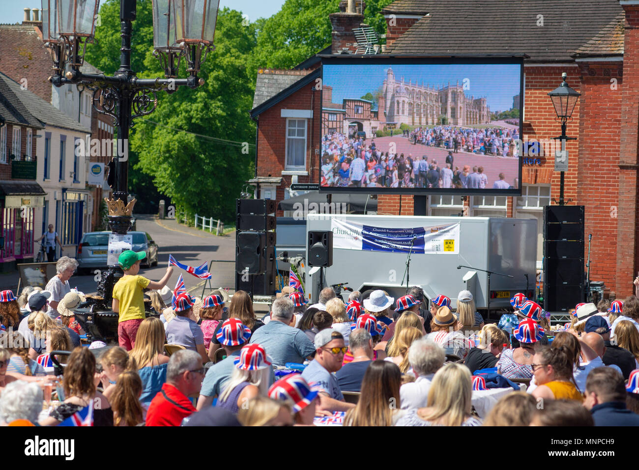 Auf einer Straßenparty auf dem Marktplatz versammeln sich Menschen, um auf einer Großleinwand zuzuschauen und die königliche Hochzeit von Prinz Harry und Meghan Markle zu feiern. Ringwood, Hampshire, England, Großbritannien, 19.. Mai 2018. Stockfoto