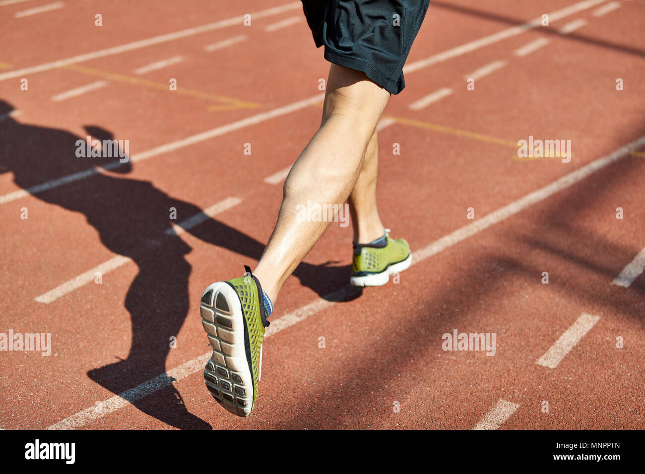 Beine und Schatten eines männlichen Athleten laufen auf der Strecke. Stockfoto