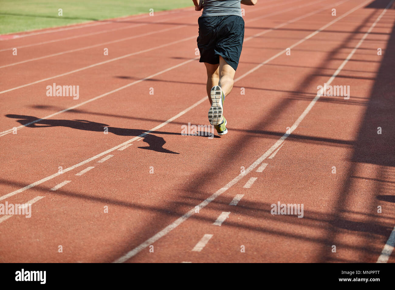 Beine und Schatten eines männlichen Athleten laufen auf der Strecke. Stockfoto