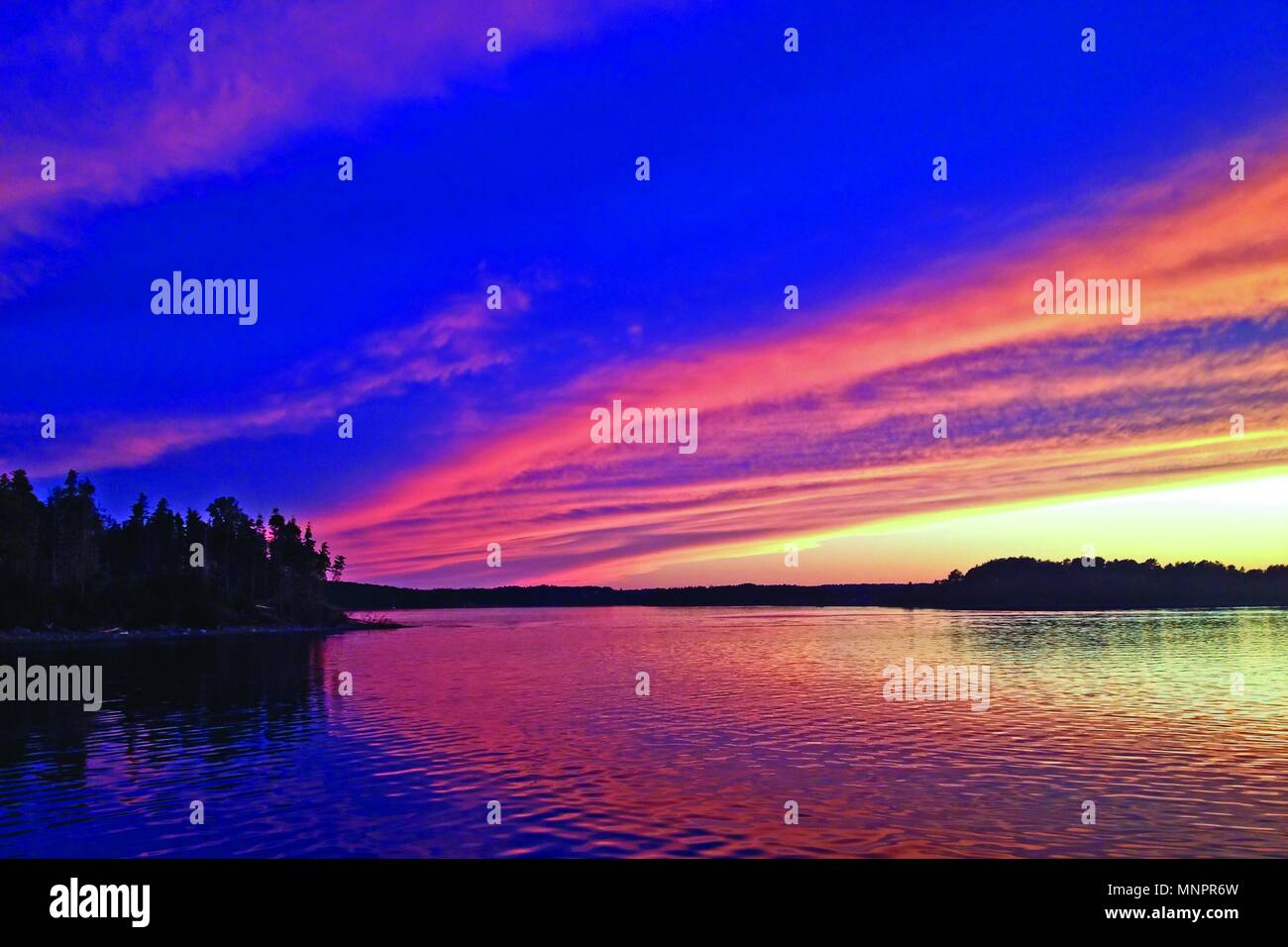 Reiche, lebhafte Pink, Lila und Gelb Farben Beleuchten Sie den Himmel wie Feuer über dem Meer. Stockfoto