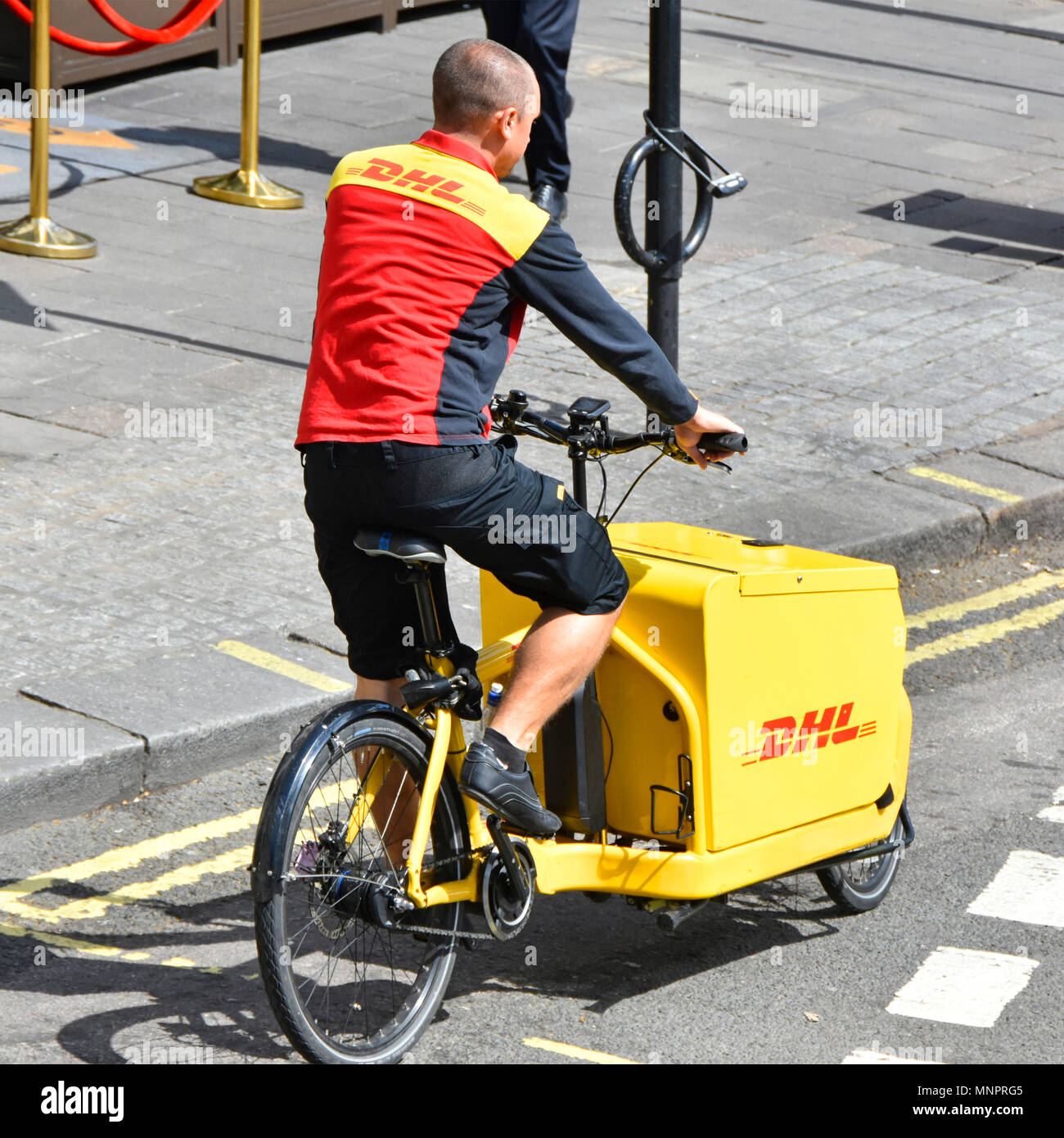 DHL Paketzusteller Mann in Uniform arbeitet am Radfahren entlang der Straße auf Frachtgut Tretrad ungewöhnliche Arbeit Lieferung von Paketen London UK Stockfoto