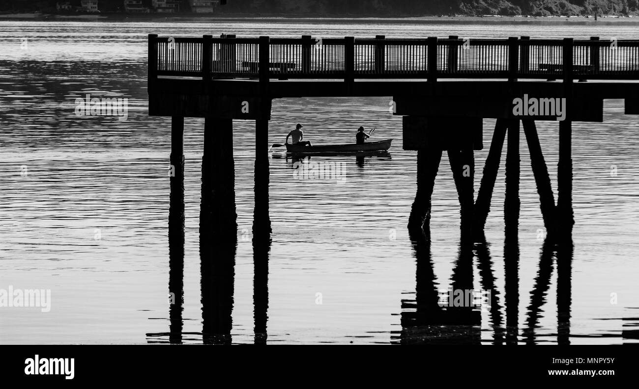 Schwarze und weiße minimalistische Szene von einem Hafen mit einem Kanu unter einem Pier im Wasser Stockfoto