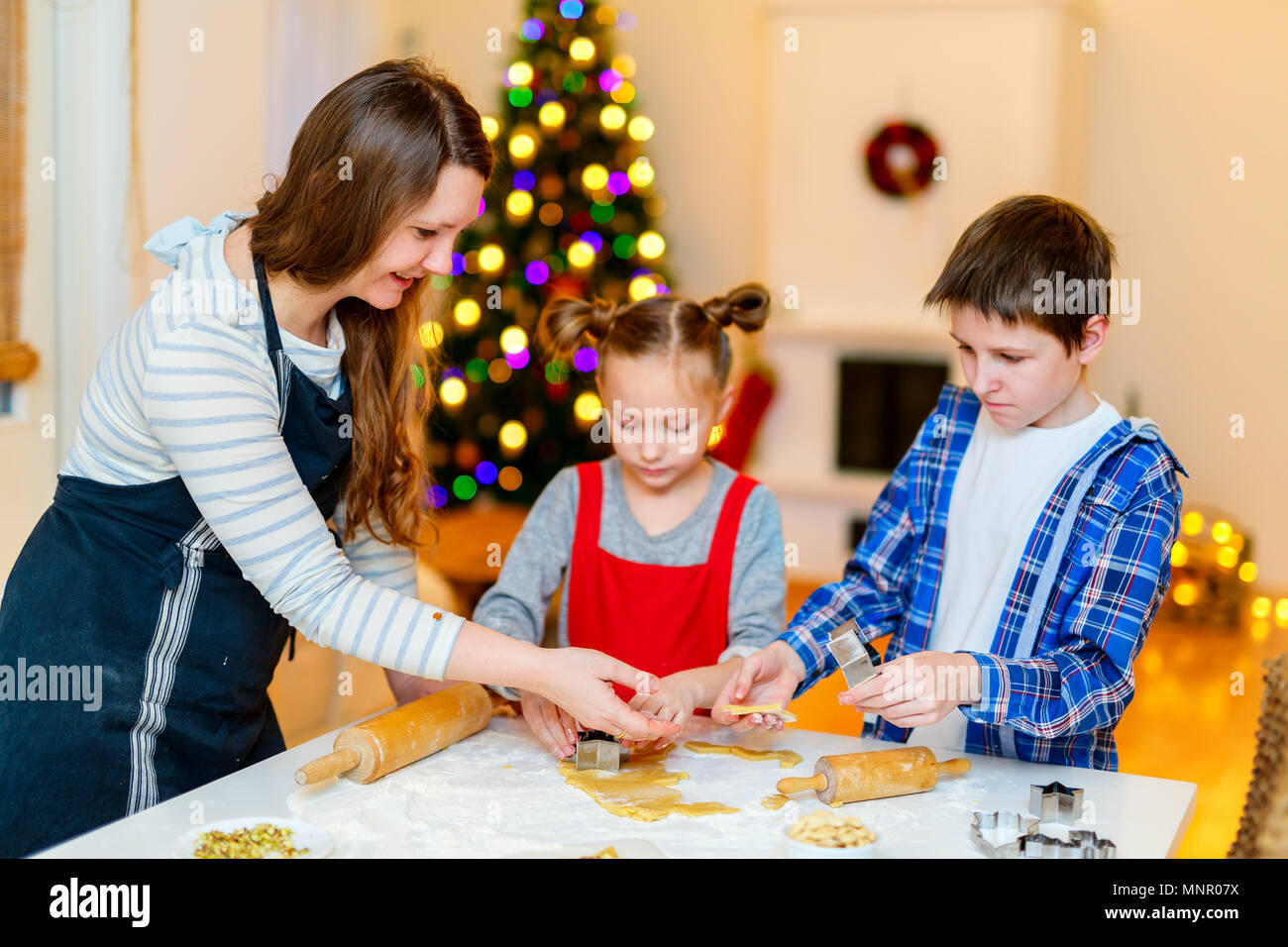 Familie von Mutter und Kinder Plätzchen backen zu Hause am Heiligabend. Schön dekoriertes Zimmer, Weihnachtsbaum und Leuchten für den Hintergrund. Stockfoto