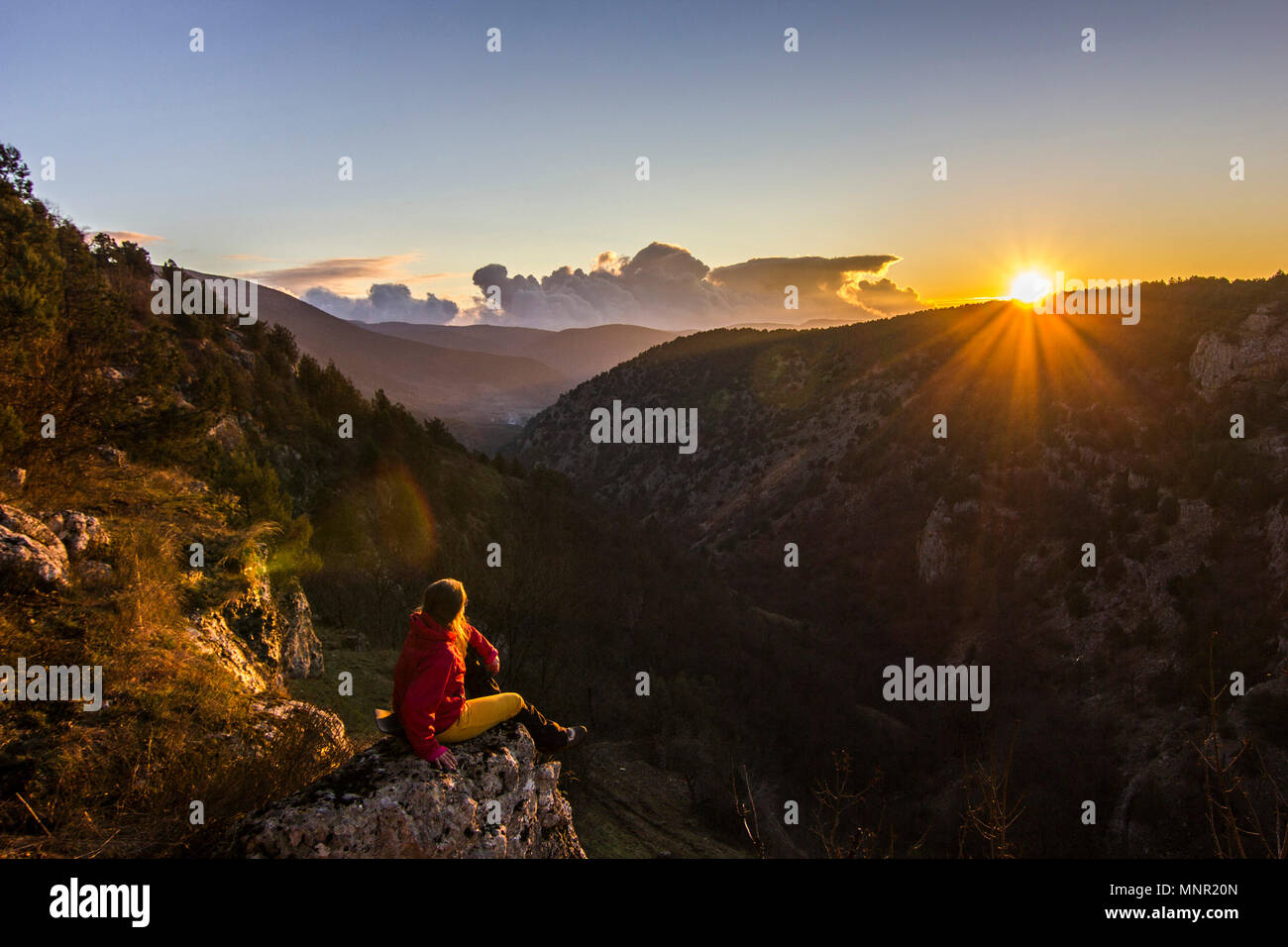 Mädchen sitzt auf einem Kliff in Berge bei Sonnenuntergang Stockfoto