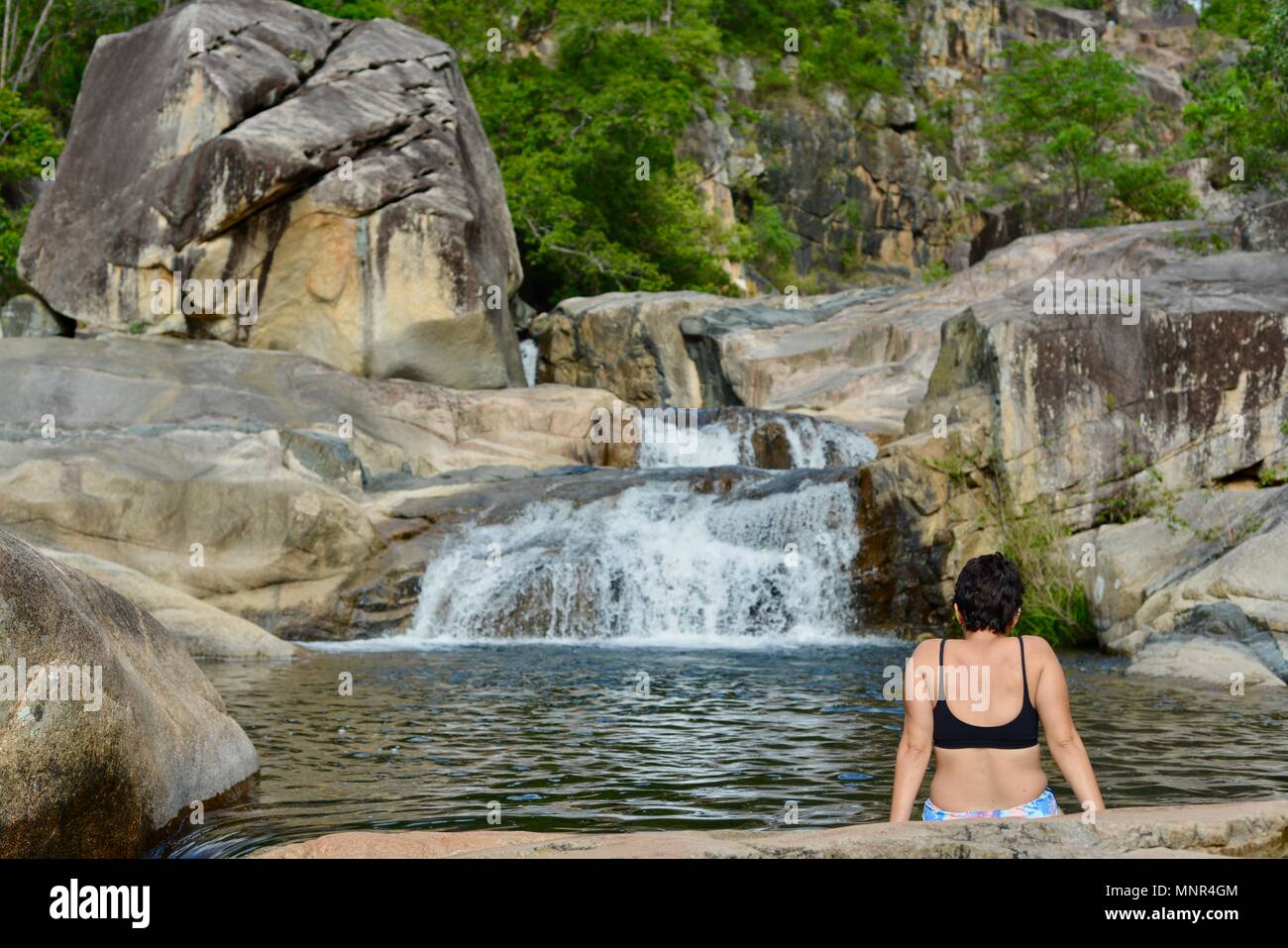 Eine Frau sitzt, indem Sie sich einen Wasserfall, Jourama Falls, Bruce Hwy, Yuruga QLD, Australia Stockfoto