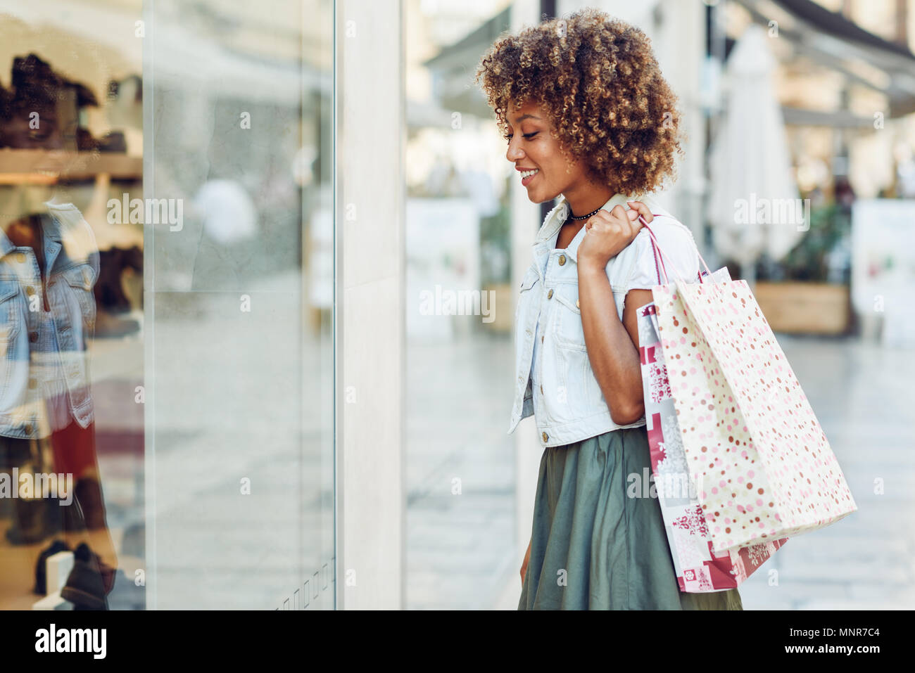 Junge schwarze Frau vor einem Schaufenster in einer Einkaufsstraße. Afrikanisches Mädchen mit Afro Frisur legere Kleidung. Stockfoto