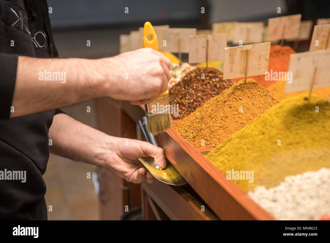 Männliche Kaufmann verwendet Pinsel überschüssige Gewürze aus der Seite des Containers in Istanbul, Spice Bazaar in der Türkei ordentlich Stockfoto