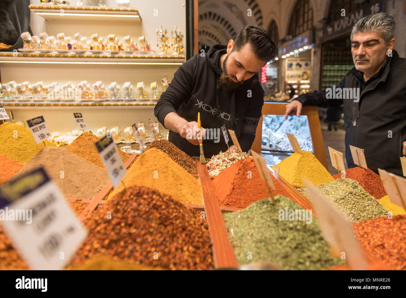 Männliche Kaufmann verwendet Pinsel überschüssige Gewürze aus der Container ordentlich wie ein erwachsener Mann sieht ihm in Istanbul, Spice Bazaar in der Türkei Stockfoto