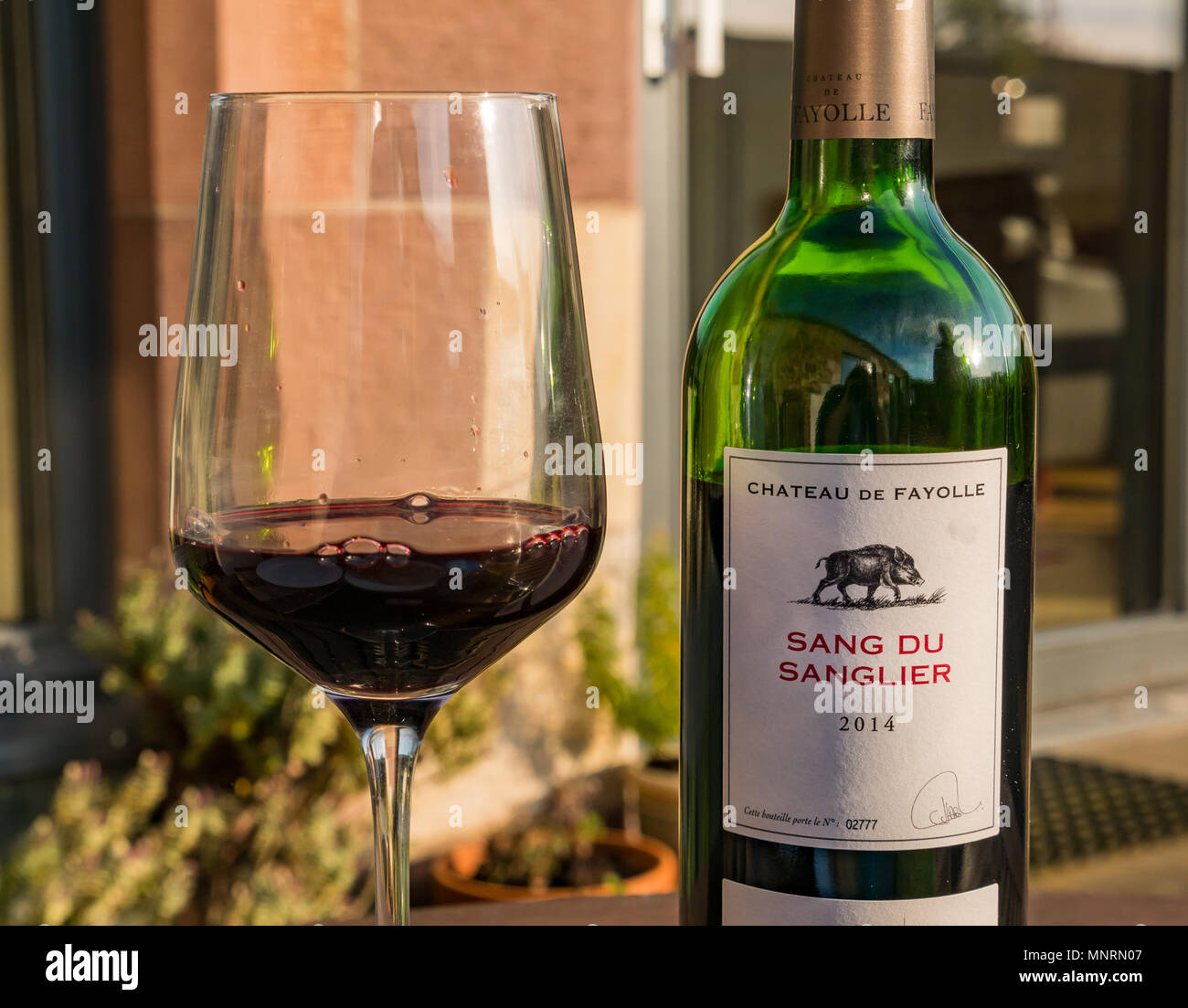 Eine Flasche französischen Rotwein, Sang du Sanglier 2014, Chateau de Périgueux, mit Wein im Glas auf Tisch im Freien in Abend sonnenbeschienenen Garten Stockfoto
