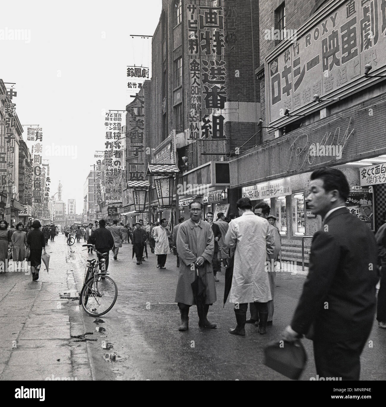 1950, historische, Außenansicht, eine Fußgängerzone in der Innenstadt  Straße in Tokio, Japan, mit dem Roxy auf der rechten Seite. Frühling und  rainmacs und Sonnenschirme werden als schauerwetter ein gemeinsames  Auftreten in der
