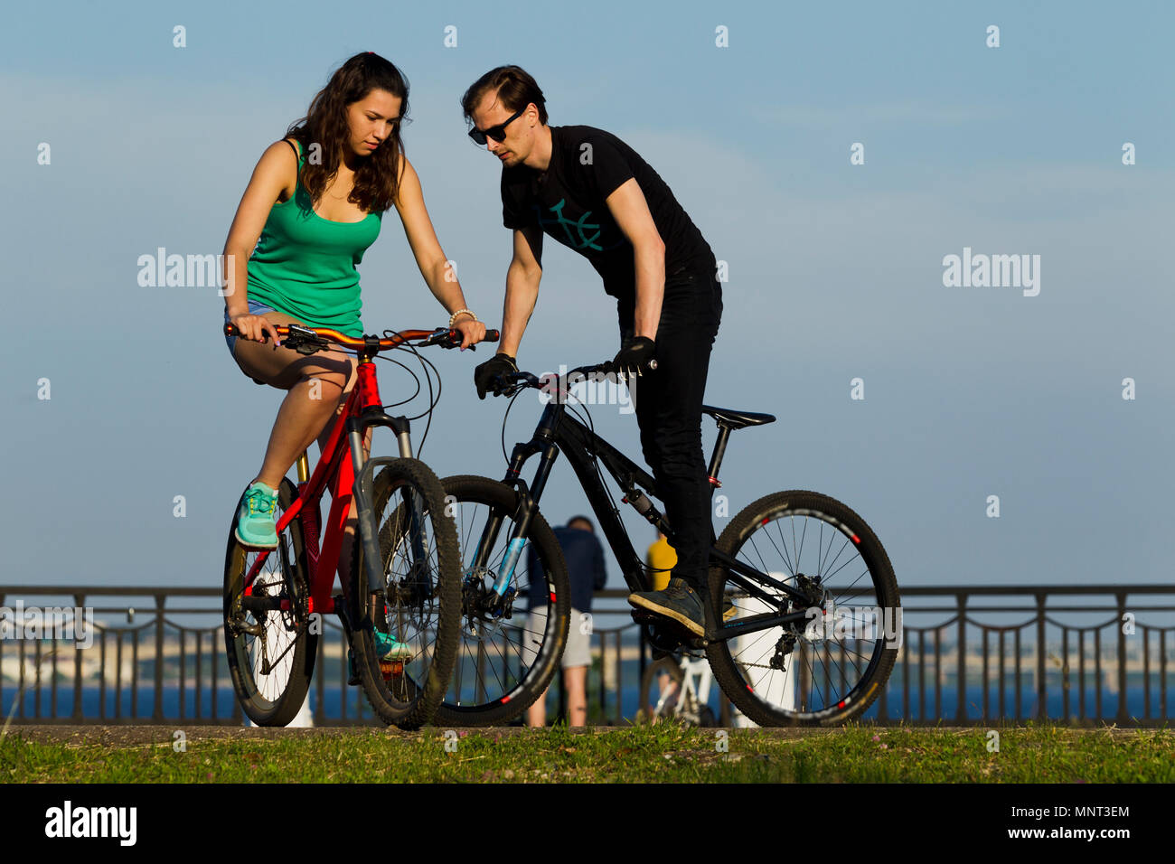Das Mädchen und der junge Mann auf einem Fahrrad in der Stadt, beleuchtet durch Sonnenlicht Stockfoto