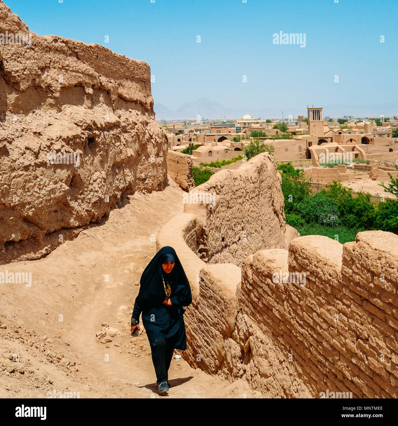 Yazd, Iran - 26. April 2018: iranische Frau das Tragen einer Tracht, bekannt als tschador, Spaziergänge auf einem Hügel mit der Stadt Yazd im Hintergrund Stockfoto