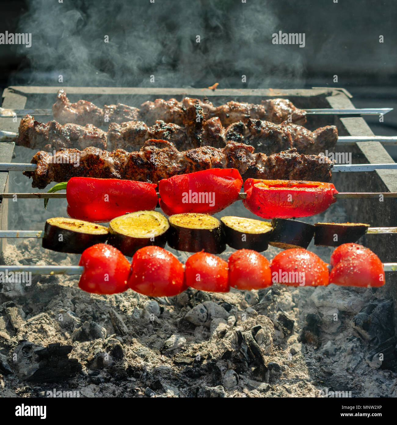 Fleisch vom Grill oder Shish Kebab und Gemüse Prozess des Kochens. Gebraten auf die Spieße auf den heißen Holzkohlengrill. Traditionelles Essen für ein Picknick. Close-up. Stockfoto