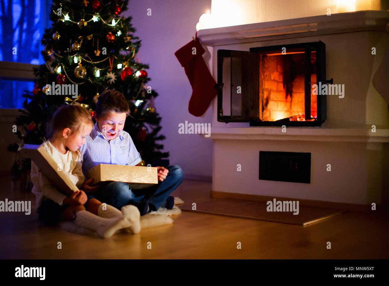 Kleine Kinder Eröffnung präsentiert neben dem Baum und Kamin in ein gemütliches Zuhause Weihnachten feiern. Stockfoto