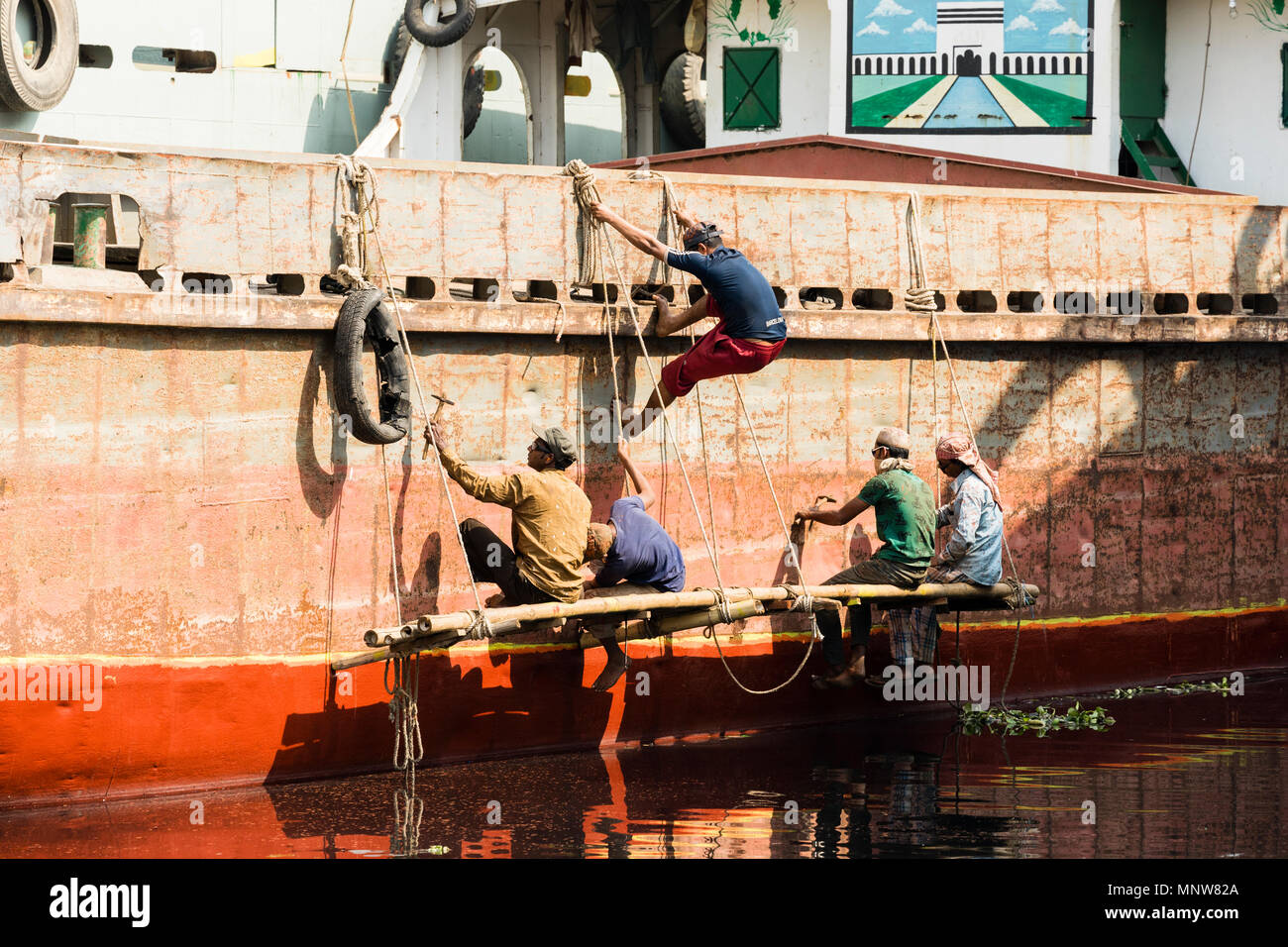 Dhaka, Bangladesh, 24. Februar 2017: Maler auf einer Werft in Dhaka sitzen auf einem Holzbrett und tragen auf dem Rumpf eines Schiffes auf dem Rostschutz Stockfoto