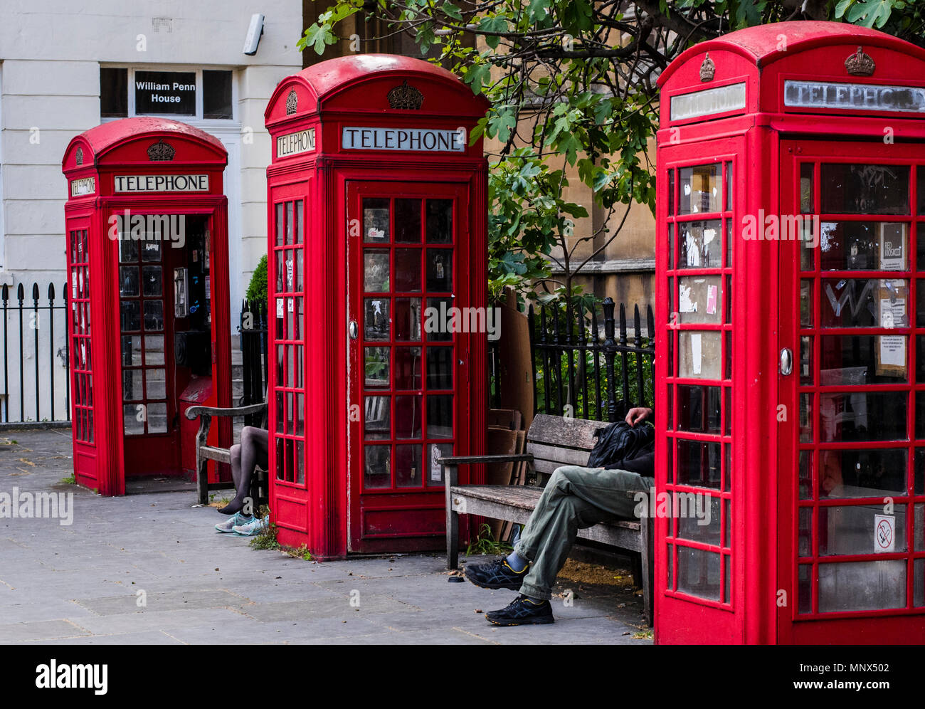 Mann und Frau, sitzen auf den Bänken zwischen roten Telefonzellen, London, England, Großbritannien Stockfoto