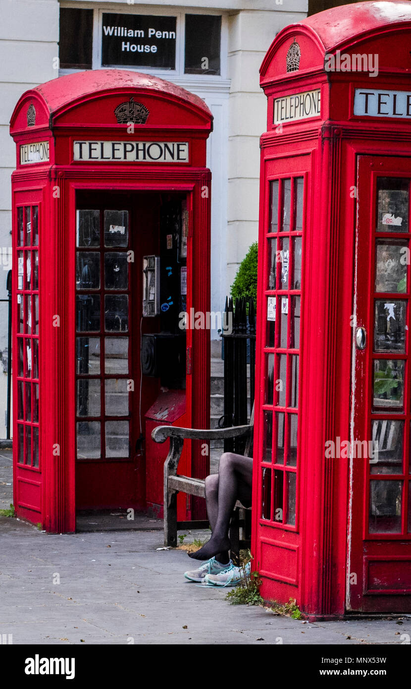 Frau sitzt auf der Bank zwischen zwei roten Telefonzellen, die Schuhe wechseln, London, England, Großbritannien Stockfoto