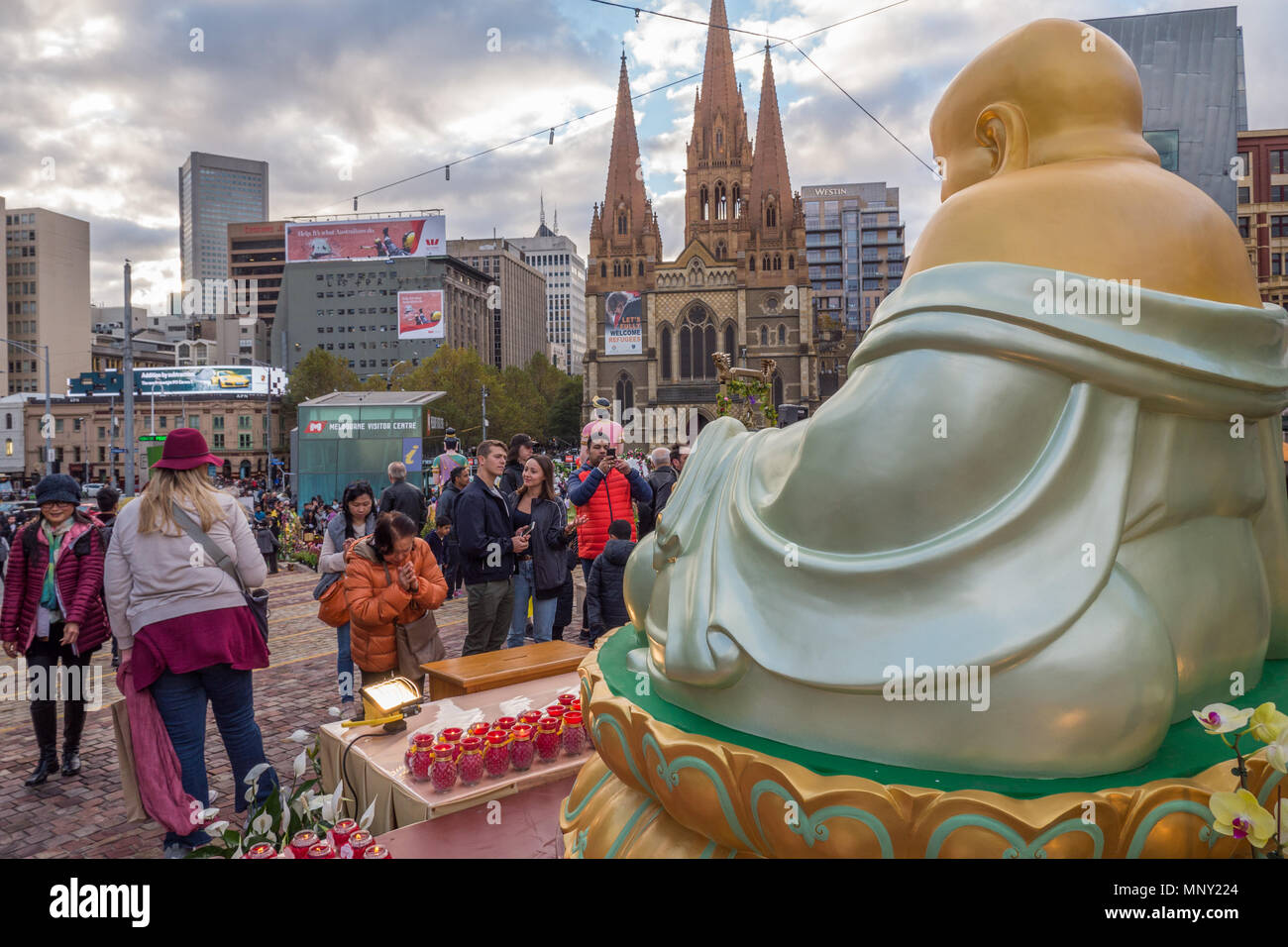 Die Leute stehen vor sehr großen Goldenen Buddha mit Melbourne Skyline im Hintergrund bei Buddha Geburtstagsfeier und multikulturellen Event. Stockfoto