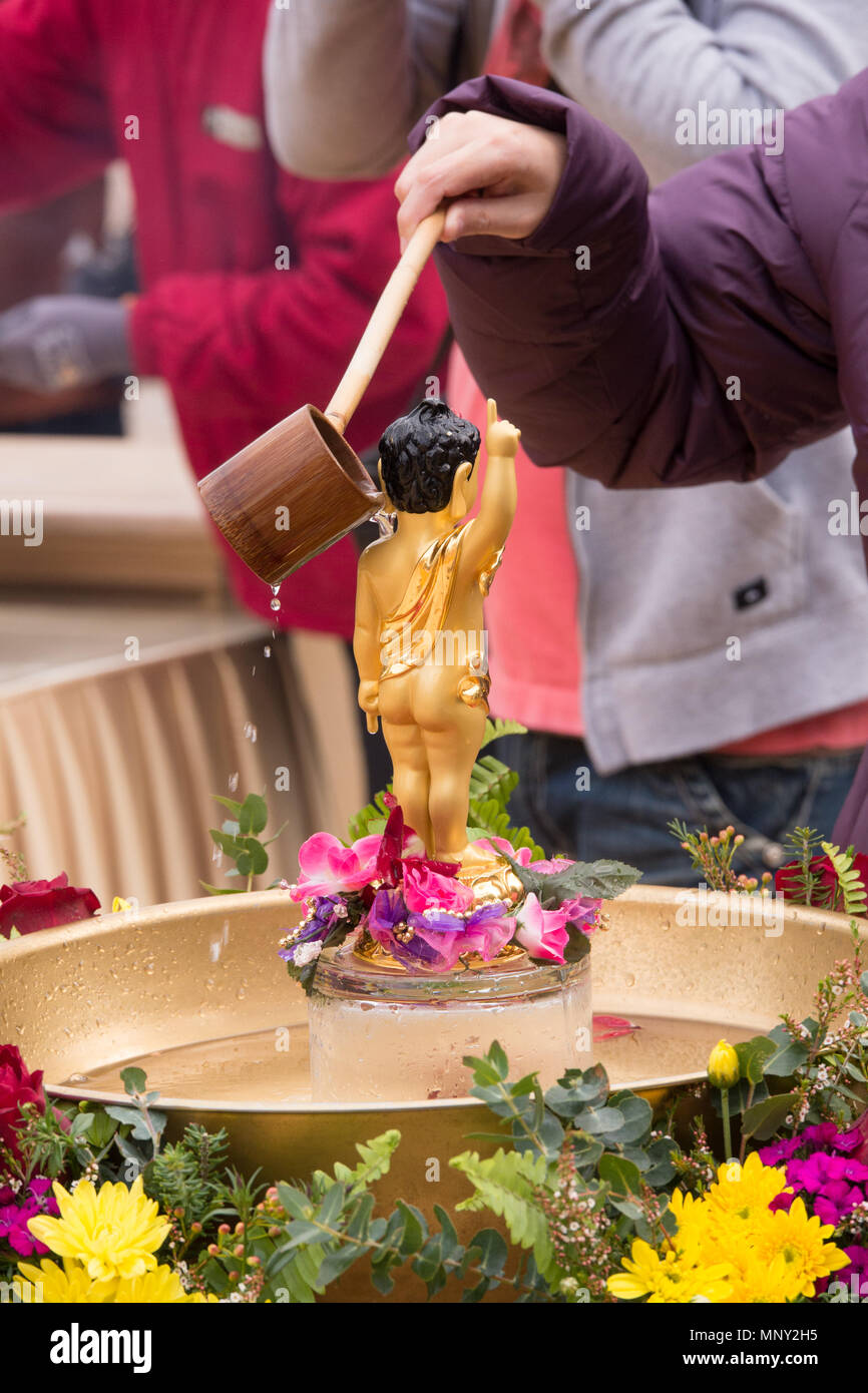 Nahaufnahme von Frau Gießen von Wasser aus einem kleinen hölzernen Löffel über die Schulter ein kleines Baby Buddha Figur, stehend auf einem bunten Lotus. Stockfoto