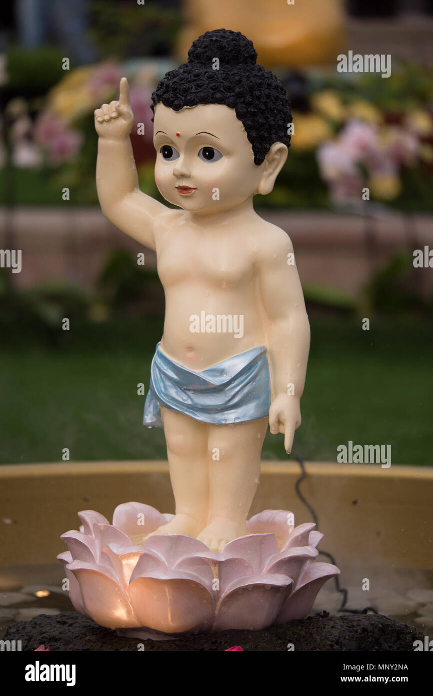 Süße kleine Baby Buddha Figur in Blau swaddle einen Arm in den Himmel hob das andere auf dem Boden stehend in Pink Lotus Blüte zeigt. Stockfoto
