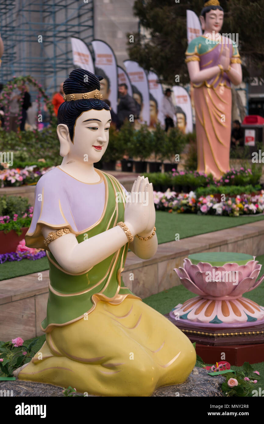 Große Plastiktüte kniende Buddha mit Gold Rock und grüne Umhüllung ineinandergelegten Hände im Gebet mit einem großen Lächeln standing Buddha und Blumen im Hintergrund. Stockfoto