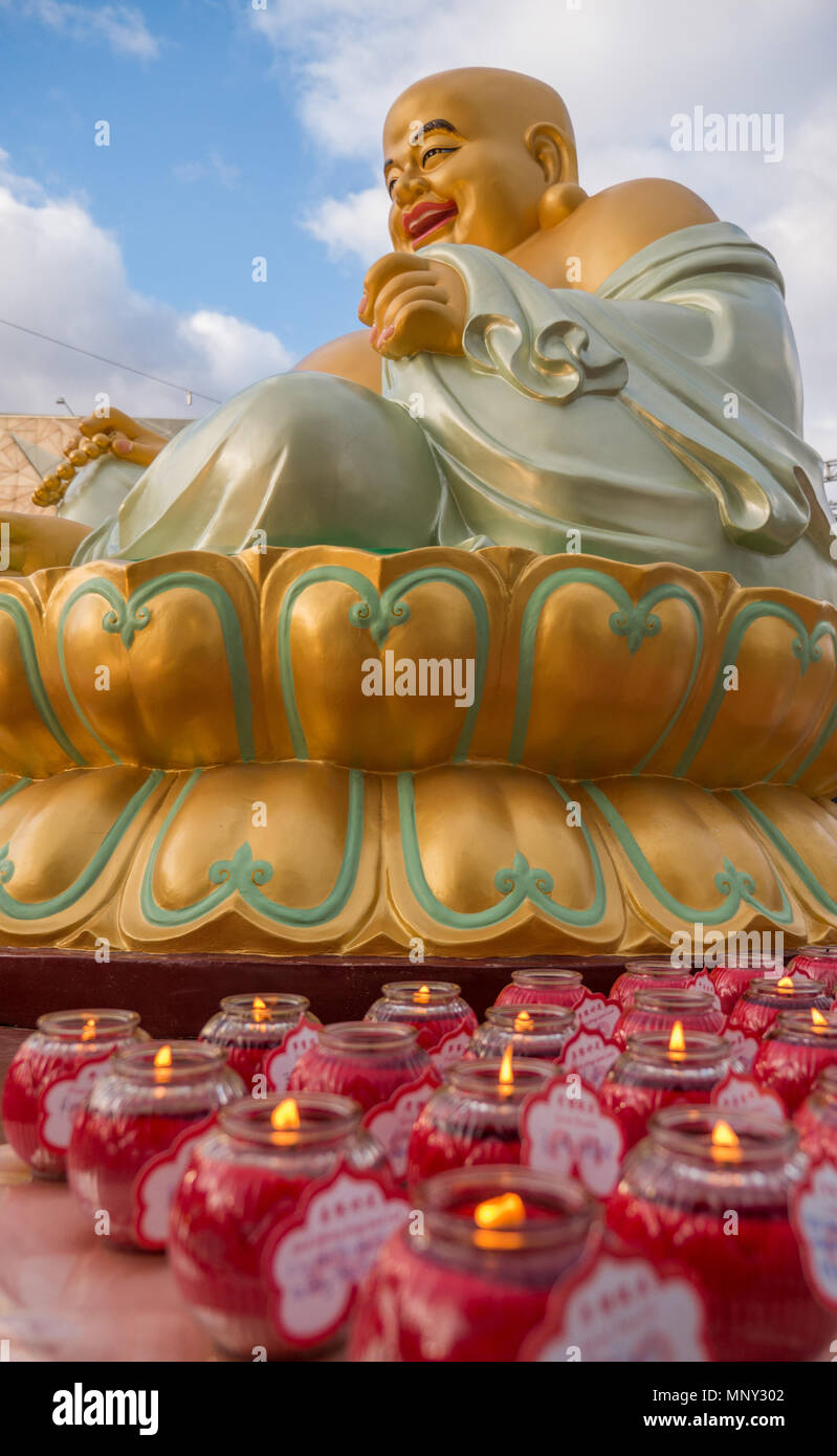 Große goldene Buddha mit großen Lächeln auf Golden Lotus, umgeben von kleinen roten Kerzen sitzt. Stockfoto
