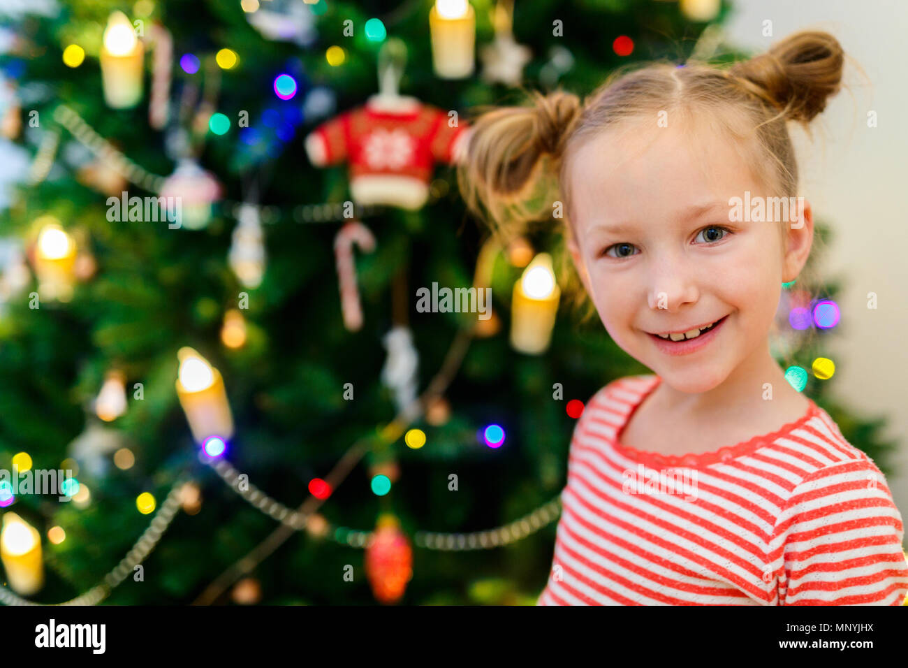 Adorable kleine Mädchen schmücken Weihnachtsbaum mit bunten Christbaumkugeln aus Glas zu Hause Stockfoto