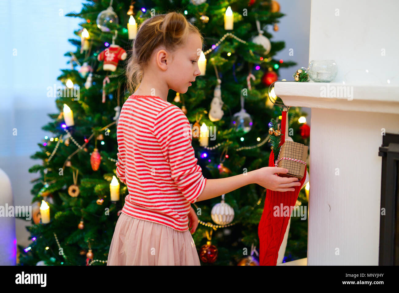 Adorable kleine Mädchen schmücken Weihnachtsbaum mit bunten Christbaumkugeln aus Glas zu Hause Stockfoto