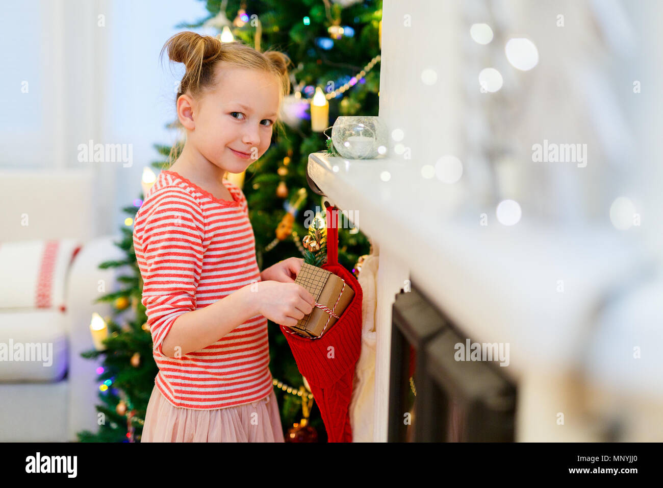 Adorable kleine Mädchen zu Hause schön für Weihnachten mit Kamin, Baum, Strümpfe und Lichtern geschmückt Stockfoto