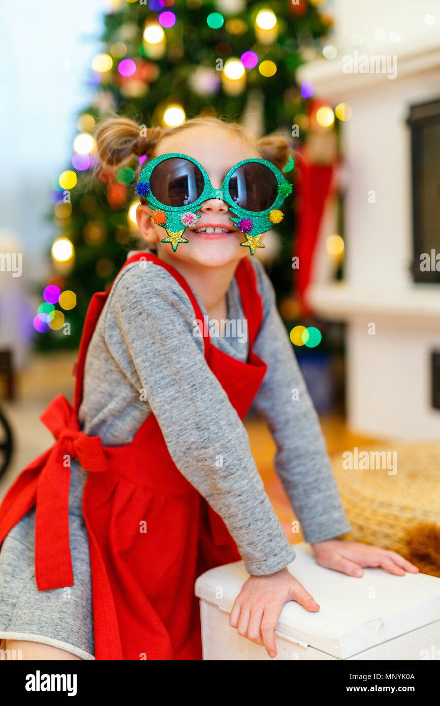 Adorable kleine Mädchen mit lustig Weihnachten Gläser in Home schön mit Weihnachtsbaum und Lichtern geschmückt Stockfoto