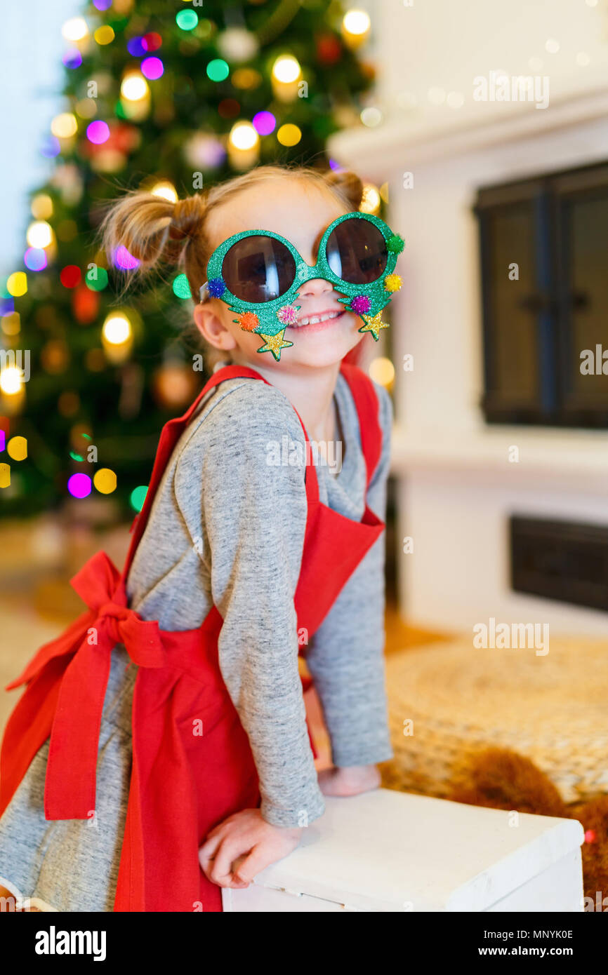 Adorable kleine Mädchen mit lustig Weihnachten Gläser in Home schön mit Weihnachtsbaum und Lichtern geschmückt Stockfoto