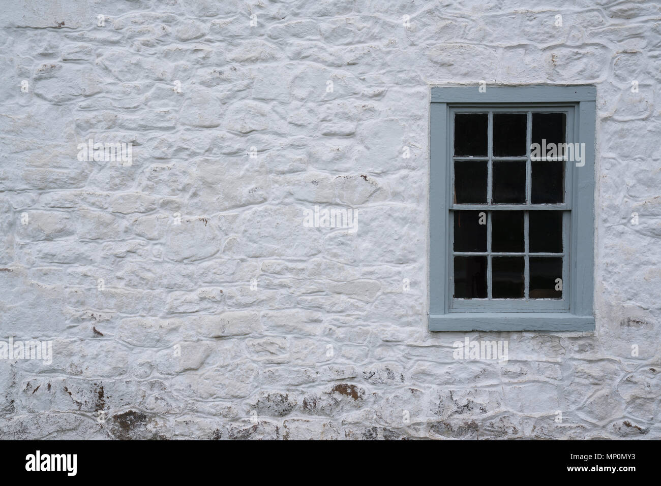 Alte graue Fenster auf einem Stein weiß getünchten Häuschen Stockfoto