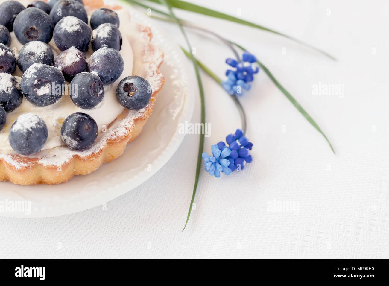 Frische Heidelbeeren Törtchen mit Vanillepudding in Teil Platte close-up, neben eleganten blauen Blüten. Lecker und gesund Sommer berry Dessert., für Hintergrund Stockfoto