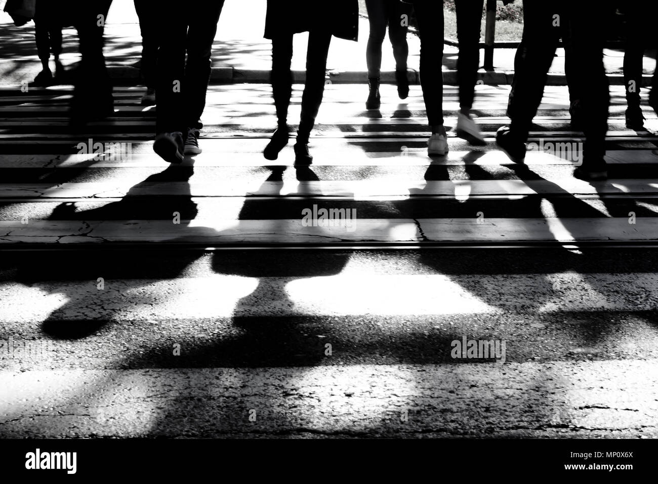 Verschwommene Silhouetten und Schatten der Menschen über die Straße am Zebrastreifen in Schwarz und Weiß, nur Beine, unkenntlich. Stockfoto