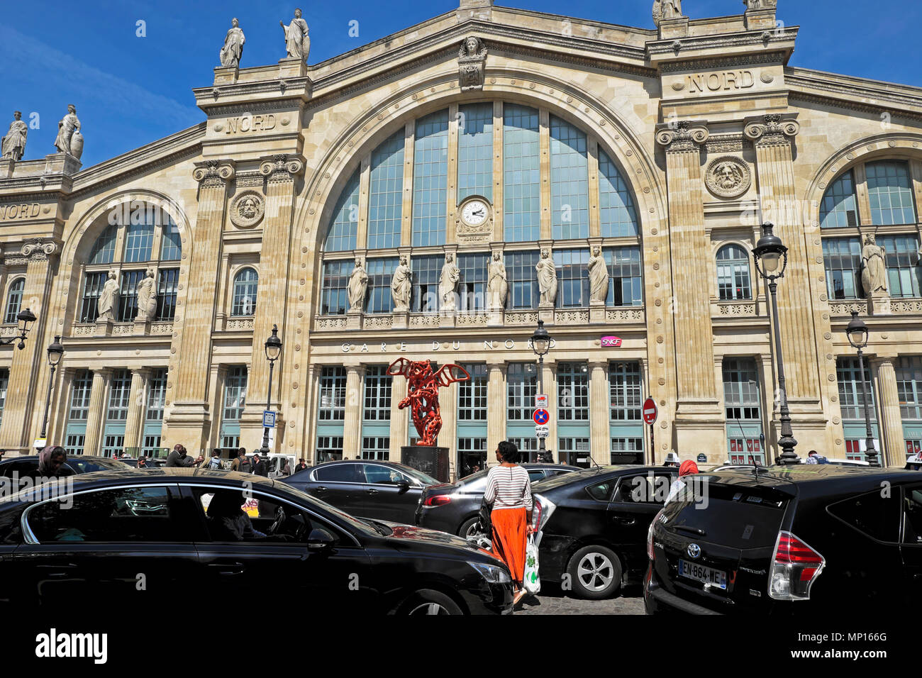 Eine Frau im orangefarbenen Rock überquert die Straße zwischen dem belebten Autoverkehr an der Fassade des Bahnhofsgebäudes Gare du Nord im Frühling Paris Frankreich KATHY DEWITT Stockfoto
