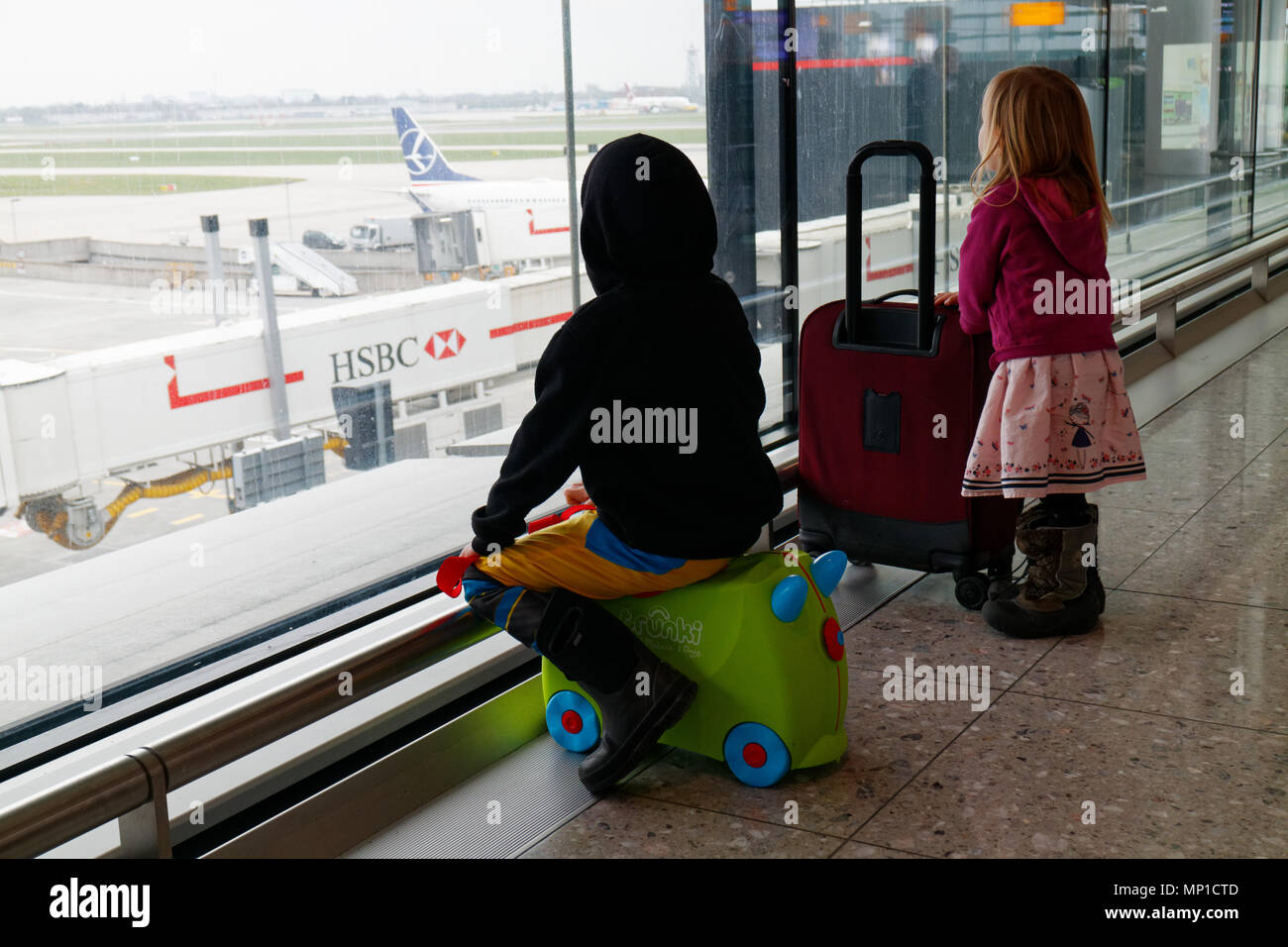 Zwei Kinder (5 und 3 Jahre alt, Bruder und Schwester) mit ihren Koffer heraus aufpassen durch das Fenster am Flughafen London Heathrow Stockfoto